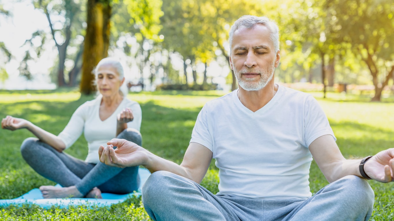 Yoga im Park. Senior Paar sitzen in Lotus Pose auf grünem Gras in Ruhe und Meditation